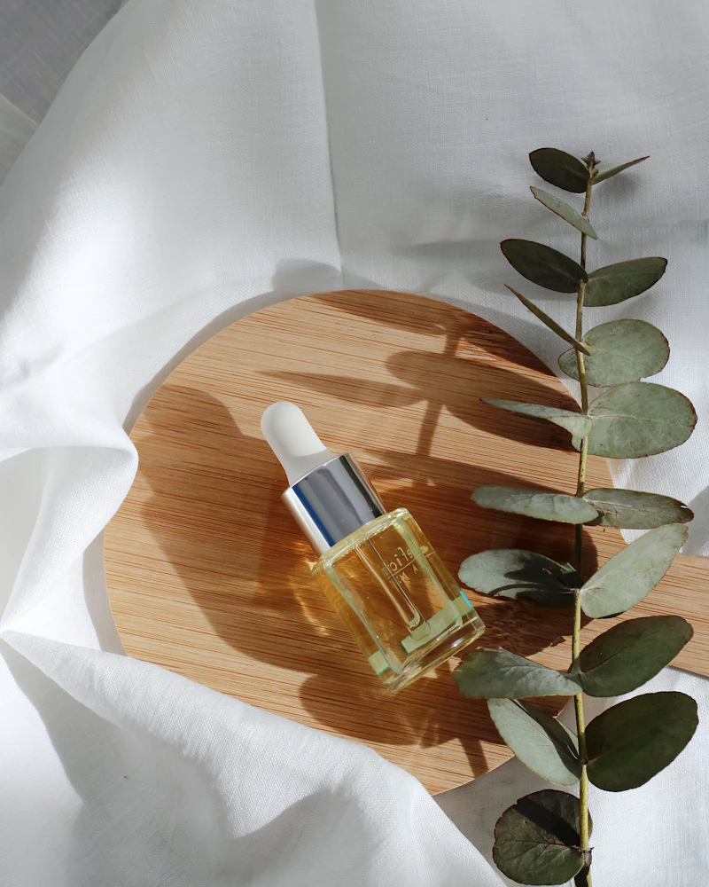 Flesje olie op een houten plankje met eucalyptus, op wit linnen